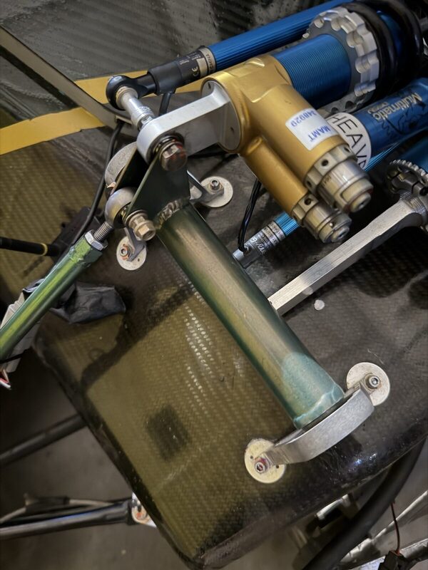 Close-up of the Multimatic damper labelled HEAVE, mounted beside the welded rocker pivot on the carbon tub.