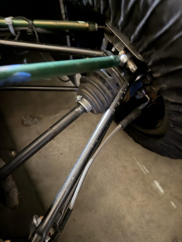 Green pushrod and toe link meeting the rear upright, with the driveshaft CV boot and tire behind.